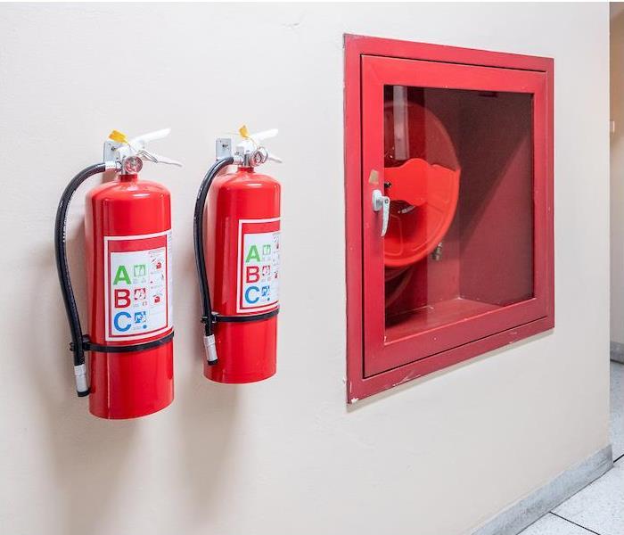 Two red fire extinguishers hanging on a wall in a commercial workplace  